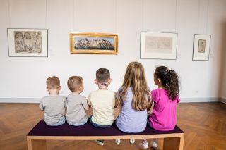 Kinder sitzen auf einer Bank und schauen sich die Kunstwerke an.