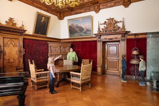 Mann mit drei Kindern im historischen Wohnzimmer von Herzog Georg II. im Schloss Elisabethenburg, die den Raum und die ausgestellten Kunstwerke betrachten.