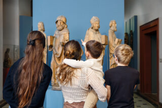 Eine Familie betrachtet Skulpturen im Schloss Elisabethenburg; ein kleiner Junge auf dem Arm seiner Mutter zeigt auf eine der Figuren.