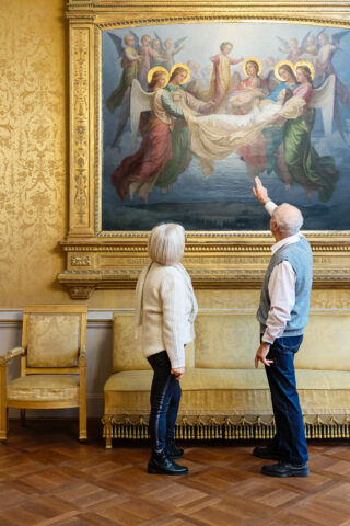 Ein älteres Besucherpaar betrachtet ein Gemälde in einem historischen Raum des Schlosses Elisabethenburg; der Mann zeigt auf das Bild.