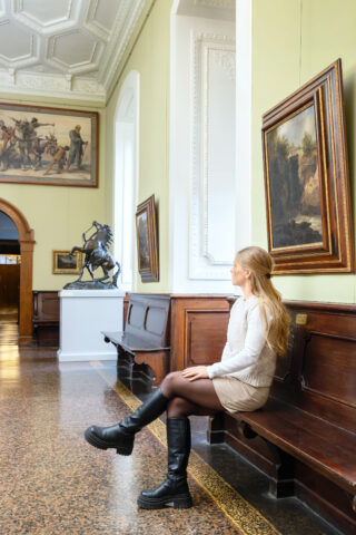 Eine Besucherin sitzt auf einer Bank im Flur des Schlosses Elisabethenburg.