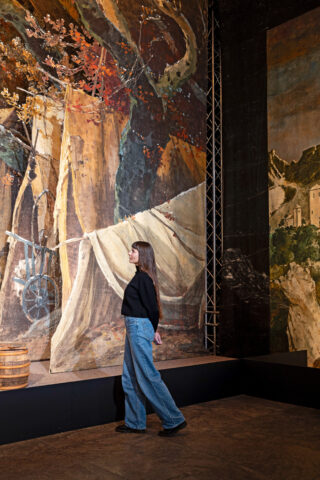 Eine junge Frau steht vor einem historischen Bühnenbild im Theatermuseum.