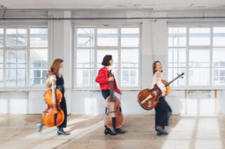 Drei Frauen des Ensembles TIEFSAITS gehen von links nach rechts und tragen historische Streichinstrumente.